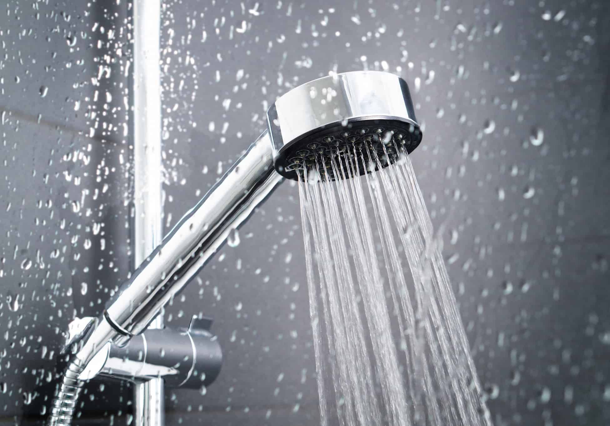 Fresh shower behind wet glass window with water drops splashing. Water running from shower head and faucet in modern bathroom.